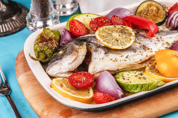 Mediterranean dish, Georgian recipe. Baked river fish with lemon, vegetables, pepper and grilled tomatoes with spices.