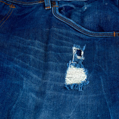 fragment of blue jeans fabric with a hole