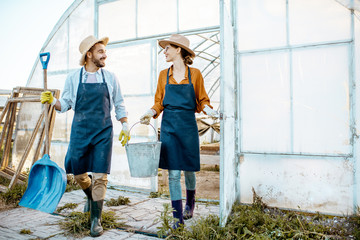 Two well-dressed farmers or agronomists walking with working tools on a farmland near the hothouse on the evening at sunset