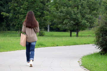 Fototapeta na wymiar Green life and ecology, slim girl in jeans walking with a paper bag in a summer park. Enjoying a nature, morning after rain