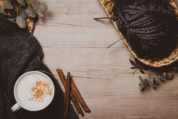 Fall winter background. Cup of cappuccino, autumn leaves, wool scarf and ball of wool yarn  on a wooden background. Home hobbies, knitting. Cozy comfort concept