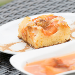 Tasty flan with apricots, cinnamon and powdered sugar. In the front there is a delicious apricot compote. Blurred background with a rattan furniture for copy space. 