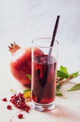 Pomegranate  juice  in glass with seeds, fruits and leaves on light marble table.