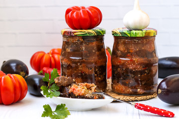 Eggplants in acute sauce of pepper, tomatoes and garlic in jars on the table, harvest for the winter