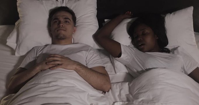 Multi-ethnic couple lying in bed together. Man suffers from his partner snoring in bed. Couple lifestyle and people health care concept.
