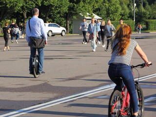 A woman on a Bicycle and a man on an electric monocycle ride on an asphalt road in the Park on a summer Sunny day, environmentally friendly urban transport © Ilya