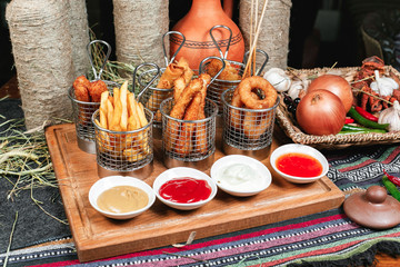 Assorted snacks on the company in the oriental style - onion rings, sausages on skewers, French fries, a set of tomato and sour cream sauces