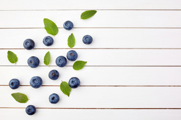 Naklejka na ściany i meble Fresh raw blueberries with leaves on white wooden background. Organic food
