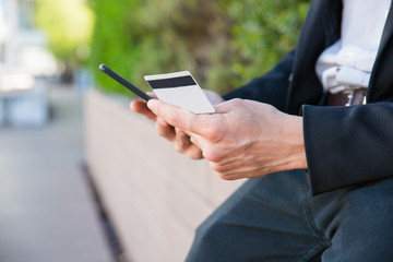 Closeup of credit card and phone in human hands. Man in office suit using smartphone and credit card for online payment. Online money transfer concept