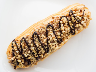 chocolate eclair sprinkled with nuts on a white plate