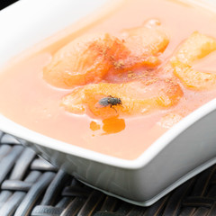 One fly sitting on an apricot in a compote. The fly is hungry and she is sucking with her proboscis apricot compote. There is a reflection of the fly in the apricot puree. 