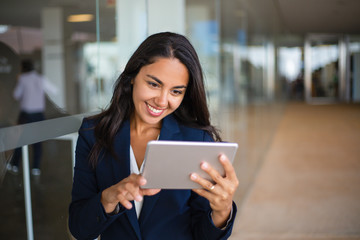Cheerful happy office worker using tablet in office hall. Young Latin business woman leaning on...