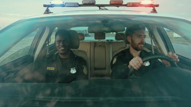 Happy friendly police officers talking and smiling while driving a police patrol car to the office at daytime. Police on duty.