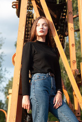 A young girl in blue jeans posing on a background of metal structures,