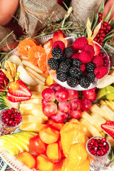 Fototapeta premium Fruit plate in Georgian style. Sliced ​​fruits - apple, banana, pineapple, orange, pear, grapes, persimmon, served with strawberries, raspberries, blackberries, blueberries in powdered sugar