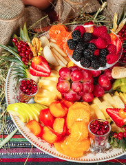  Fruit plate in Georgian style. Sliced ​​fruits - apple, banana, pineapple, orange, pear, grapes, persimmon, served with strawberries, raspberries, blackberries, blueberries in powdered sugar