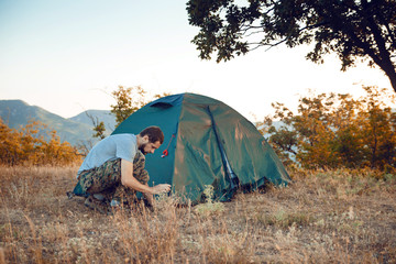 Autumn trekking in the mountains. Tourist sets up a tent