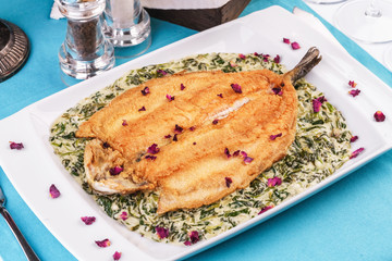 Fried steak of sea fish in batter, in a creamy sauce with greens and rose petals. Caucasian cuisine, Mediterranean food