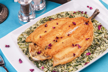 Fried steak of sea fish in batter, in a creamy sauce with greens and rose petals. Caucasian cuisine, Mediterranean food