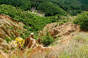 Fragment of the famous Stob’s Pyramids with unusual shape red and yellow rock formations, green bushes and trees around, west share of Rila mountain, Kyustendil region, Bulgaria, Europe  