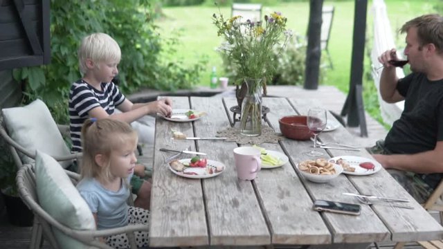 The family has lunch on the veranda in summer. Dad with children eating in the country