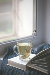 Knitted Sweater cup of hot tea Open Book on window. Cozy Winter Autumn day. Natural Light Authentic Tranquil Atmosphere. Kinfolk Hygge Slow Living Style. Matte Toned