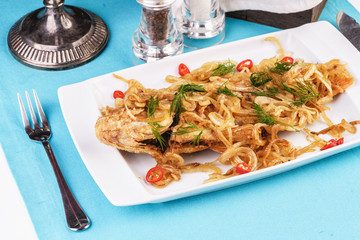 Fried sea fish pike perch is served under onion rings, chili peppers and greens according to the Georgian recipe. Mediterranean Kitchen