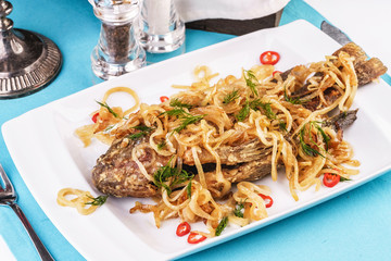 Fried sea fish pike perch is served under onion rings, chili peppers and greens according to the Georgian recipe. Mediterranean Kitchen