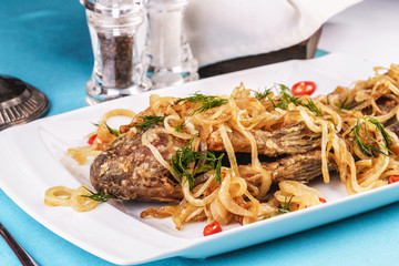 Fried sea fish pike perch is served under onion rings, chili peppers and greens according to the Georgian recipe. Mediterranean Kitchen