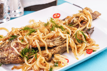 Fried sea fish pike perch is served under onion rings, chili peppers and greens according to the Georgian recipe. Mediterranean Kitchen