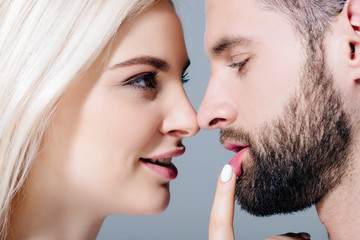 Obraz premium beautiful young woman touching lips of man with finger isolated on grey