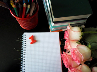 September 1 concept. Books, flowers, pencils on a black table. and white notebook. Back to school