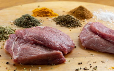 Raw uncooked slices of meat on wooden table with spices