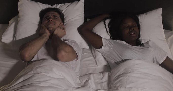 Multi-ethnic couple lying in bed together. Man suffers from his partner snoring in bed. Couple lifestyle and people health care concept.
