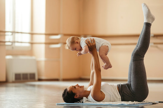 Young mother doing post-pregnancy exercises with her baby in health club.
