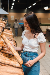 happy asian woman smiling while holding baguette in supermarket