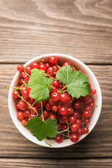Fresh ripe red currant berry in a white cup on a dark wooden background. View from above.