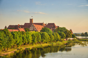 Naklejka na ściany i meble The Castle of the Teutonic Order in Malbork, Poland with the Nogat river shore. 13th-century castle is the largest castle in the world measured by land area and a UNESCO World Heritage Site