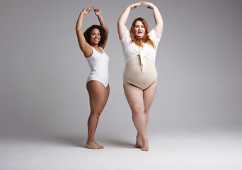 Couple of fat female friends raising their hands up in studio