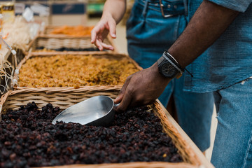 cropped view of african american man holding metal scoop with raisins near woman gesturing in supermarket