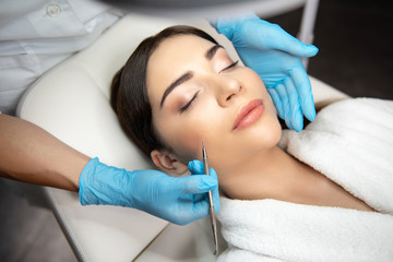 Cosmetologist in sterile gloves using blackhead remover to clean lady face