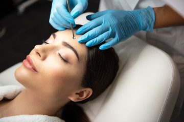 Cosmetologist in sterile gloves using blackhead remover to clean lady forehead