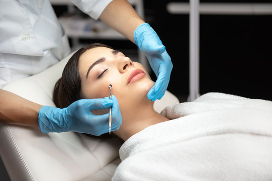 Beautician in sterile gloves using blackhead remover to clean lady face