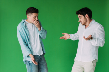 two worried men in shirts gesturing isolated on green