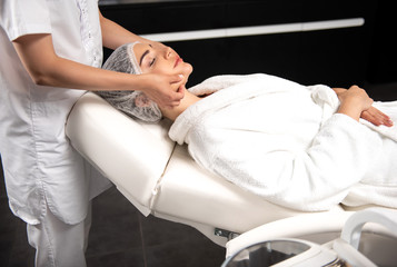 Professional masseuse massaging face of charming lady at spa salon