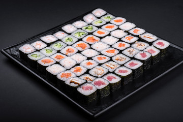 Top view assorted sushi set on a black on plate, dark background. Asian food restaurant delivery, platter set. Japanese classic seafood, nigiri, rolls, soy sauce, ginger, copy space.