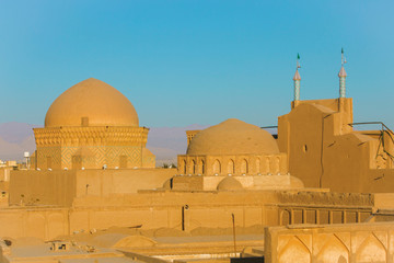 Yellow domes and minarets illuminated by the setting sun, view of mountains and roofs of the city of Yazd Iran