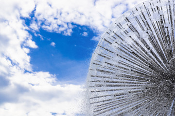 Beautiful circle fountain against blue cloudy sky. A lot of water streams. Abstract photo with copy space. Amazing background. Spraying water around.