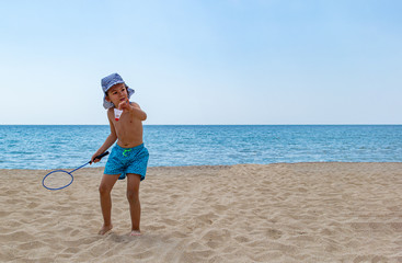 The child plays with a badminton racket and a shuttlecock on the beach. The concept of a family holiday. Copy space.