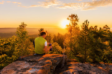 Hiker with backpack standing on a rock and enjoying sunset on mauntain